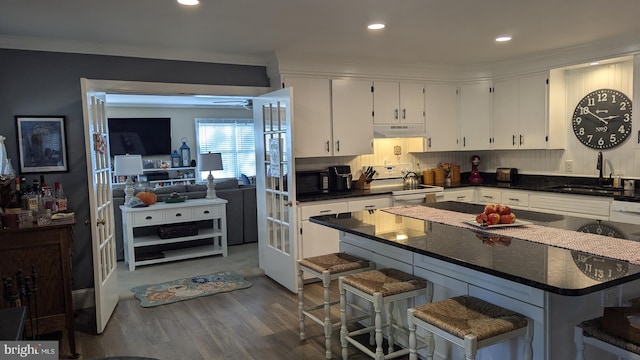 kitchen with sink, white electric stove, dark hardwood / wood-style floors, white cabinetry, and a breakfast bar area