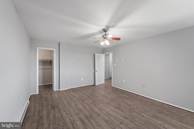 unfurnished bedroom with a baseboard heating unit, a walk in closet, dark hardwood / wood-style flooring, a closet, and ceiling fan