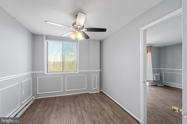 spare room featuring a wall mounted air conditioner, hardwood / wood-style flooring, a baseboard radiator, and ceiling fan