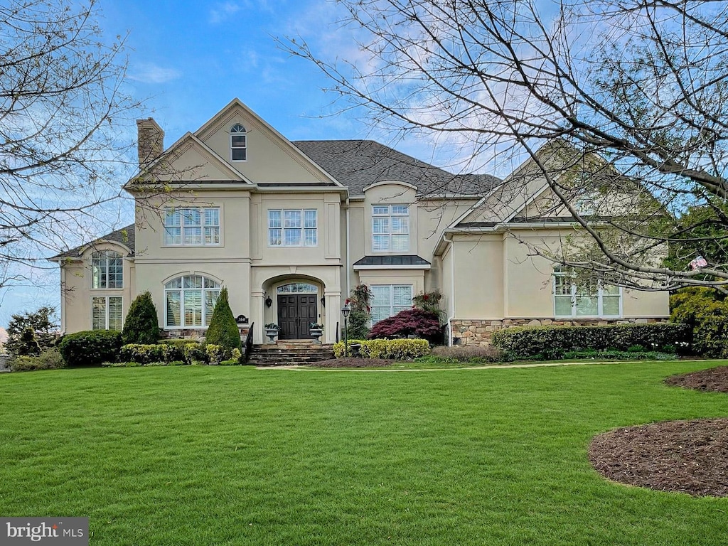 french provincial home featuring stone siding, a chimney, a front lawn, and stucco siding