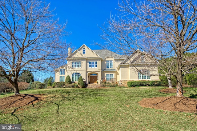 french country home with stucco siding, a front yard, and a chimney