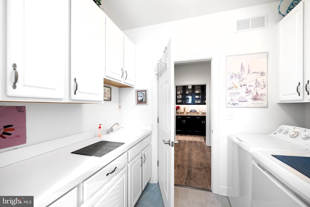 clothes washing area with light hardwood / wood-style floors, cabinets, separate washer and dryer, and sink