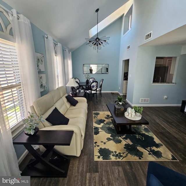 living room featuring high vaulted ceiling, dark hardwood / wood-style floors, an inviting chandelier, and a skylight