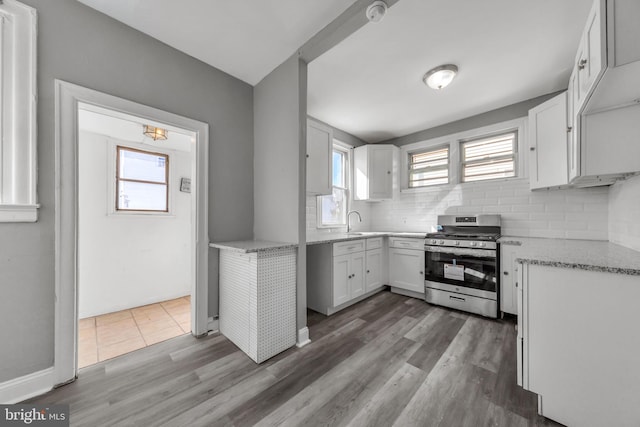 kitchen with decorative backsplash, hardwood / wood-style flooring, stainless steel range, sink, and white cabinets