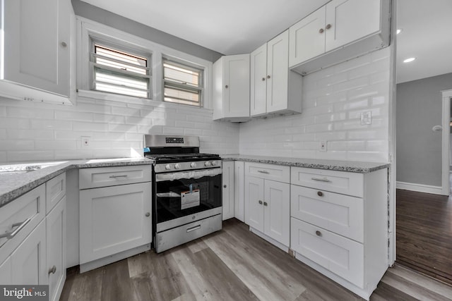 kitchen with light wood-type flooring, stainless steel gas stove, white cabinetry, light stone counters, and decorative backsplash