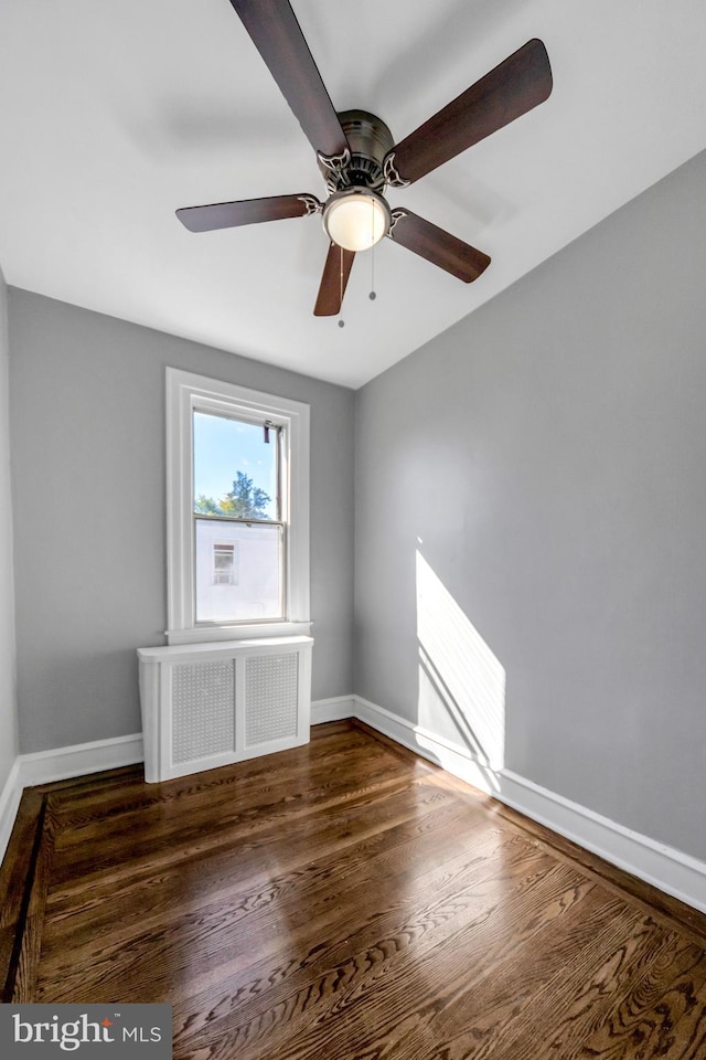 spare room with dark hardwood / wood-style floors, radiator, and ceiling fan