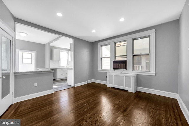 unfurnished living room featuring dark wood-type flooring, radiator heating unit, plenty of natural light, and sink