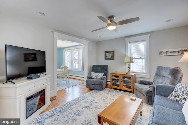 living room with ceiling fan, light wood-type flooring, and a baseboard heating unit