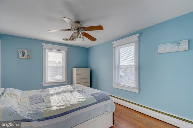 bedroom featuring ceiling fan, light wood-type flooring, multiple windows, and a baseboard heating unit