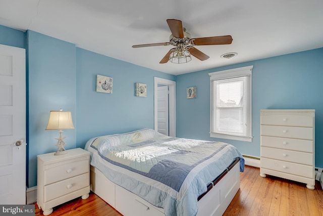 bedroom with a baseboard heating unit, hardwood / wood-style floors, and ceiling fan