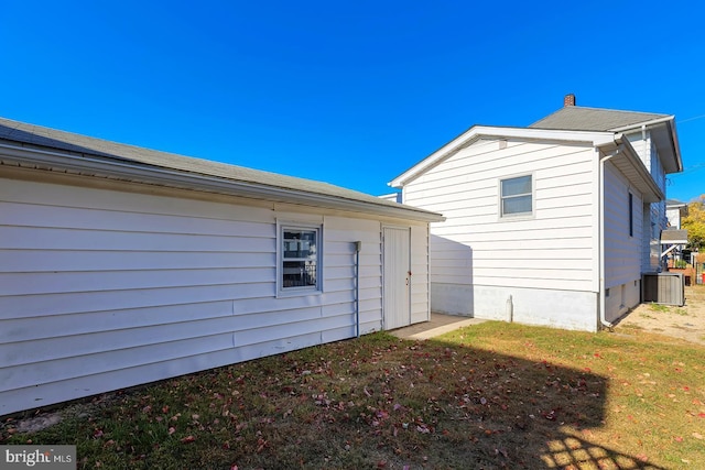 rear view of house featuring central AC unit and a lawn