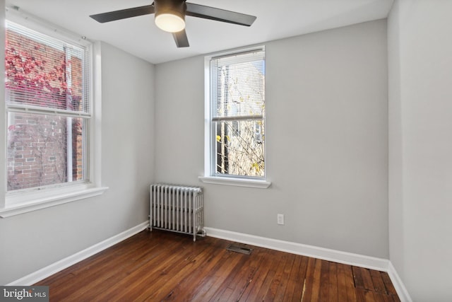 empty room with dark hardwood / wood-style floors, ceiling fan, and radiator