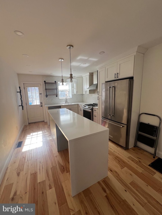 kitchen featuring white cabinetry, appliances with stainless steel finishes, hanging light fixtures, a center island, and light wood-type flooring