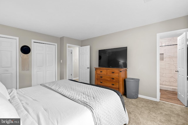 bedroom with connected bathroom, light colored carpet, and two closets