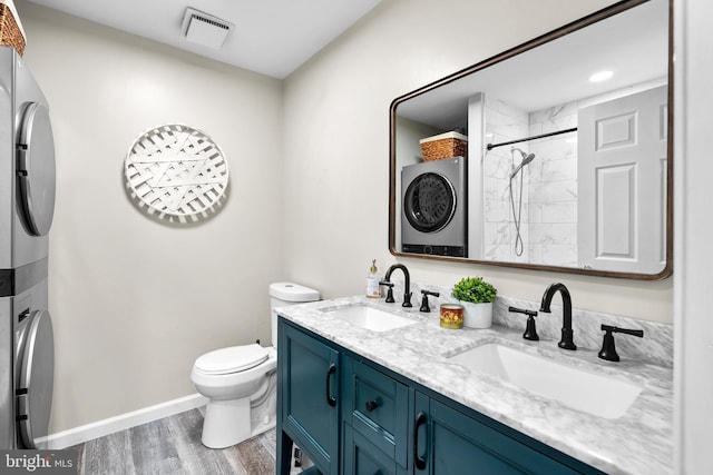 bathroom featuring vanity, tiled shower, stacked washer / dryer, hardwood / wood-style floors, and toilet