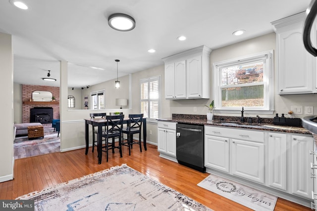 kitchen featuring a brick fireplace, stainless steel dishwasher, sink, light hardwood / wood-style flooring, and white cabinetry