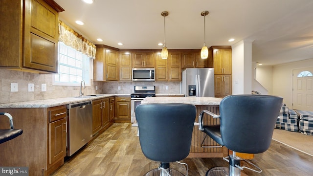 kitchen featuring stainless steel appliances, sink, decorative light fixtures, light hardwood / wood-style flooring, and a center island