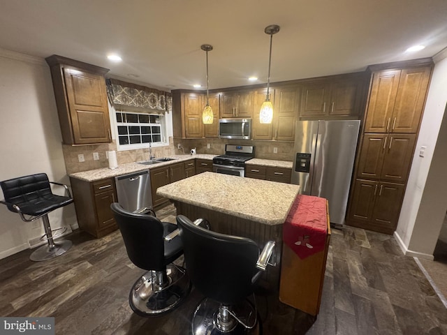 kitchen featuring appliances with stainless steel finishes, light stone counters, sink, decorative light fixtures, and a center island