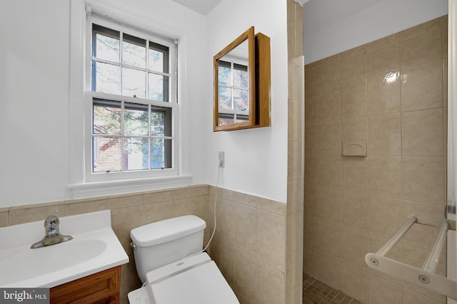 bathroom featuring tile walls, tiled shower, vanity, and toilet