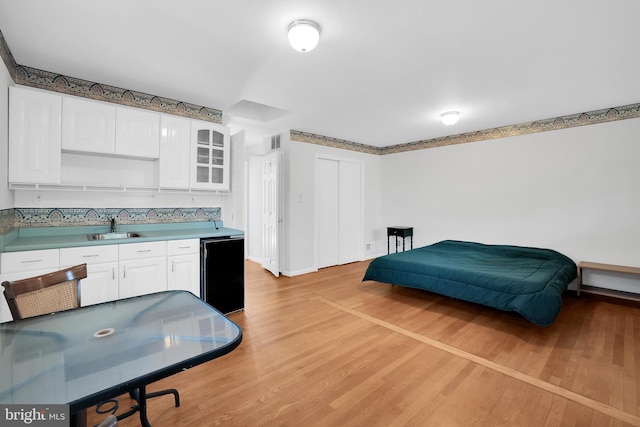 kitchen featuring white cabinets, black refrigerator, sink, and light wood-type flooring