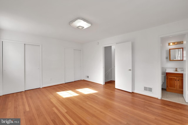 unfurnished bedroom featuring multiple closets, sink, light hardwood / wood-style floors, and ensuite bath