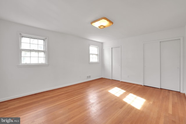 unfurnished bedroom with multiple closets, light wood-type flooring, and multiple windows