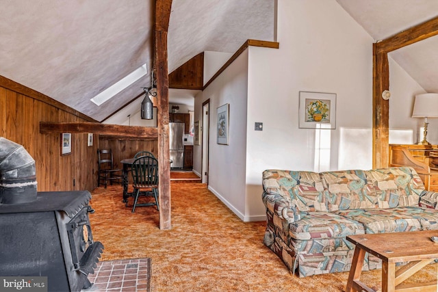 living room featuring a wood stove, light carpet, wooden walls, high vaulted ceiling, and a skylight