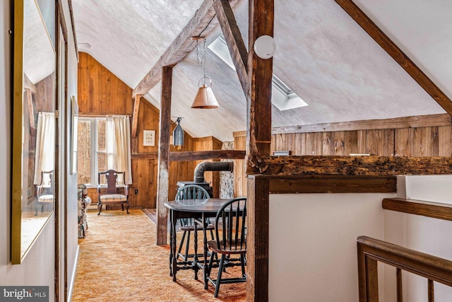 interior space featuring wood walls, light carpet, a wood stove, and lofted ceiling with skylight