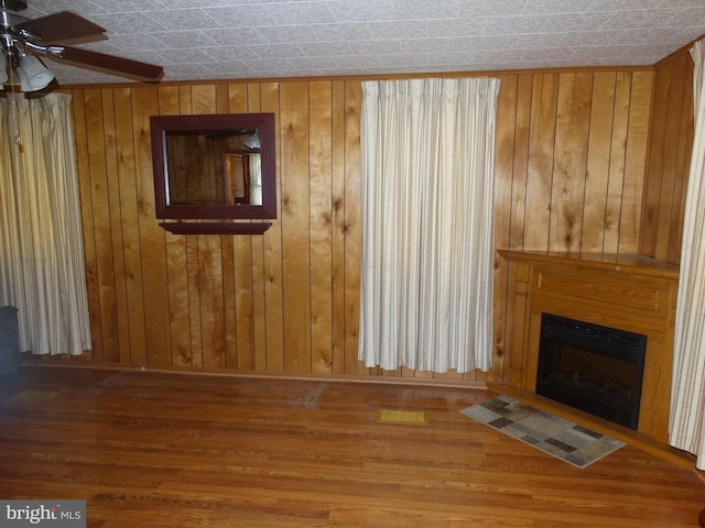 unfurnished living room with wood walls, wood-type flooring, and ceiling fan