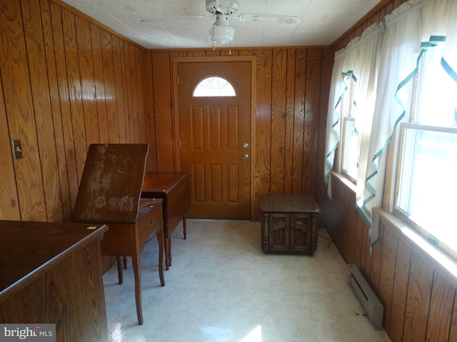 carpeted entryway with a baseboard radiator, ceiling fan, and wood walls