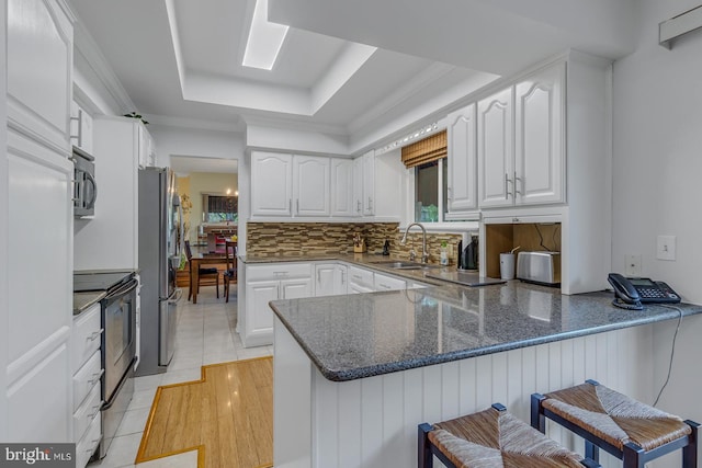 kitchen with kitchen peninsula, appliances with stainless steel finishes, a kitchen breakfast bar, white cabinetry, and a tray ceiling