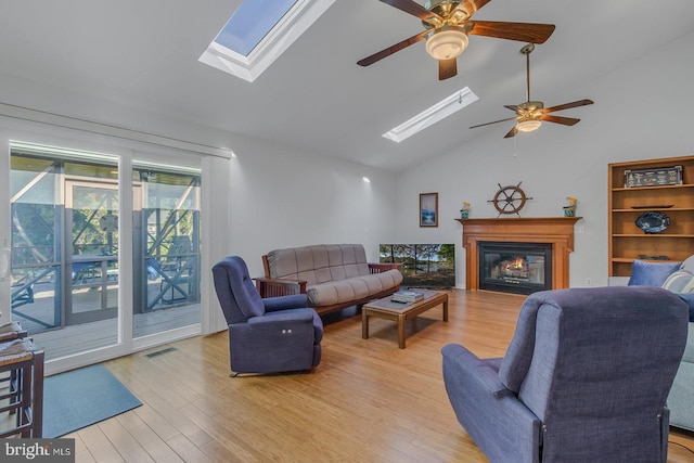 living room featuring vaulted ceiling with skylight, light hardwood / wood-style flooring, and ceiling fan