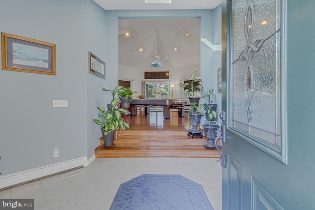 entryway with lofted ceiling with skylight, ceiling fan, and light tile patterned floors