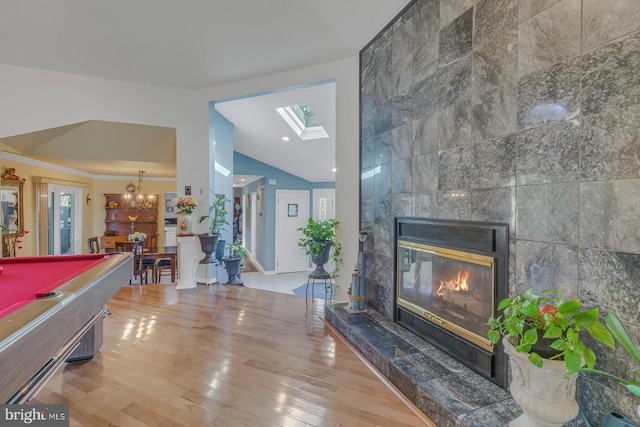 playroom featuring hardwood / wood-style flooring, a tile fireplace, vaulted ceiling with skylight, billiards, and tile walls