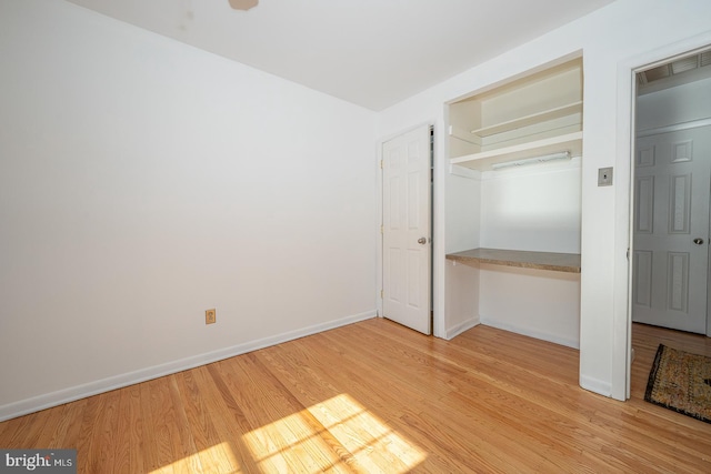 unfurnished bedroom with a closet, built in desk, and wood-type flooring