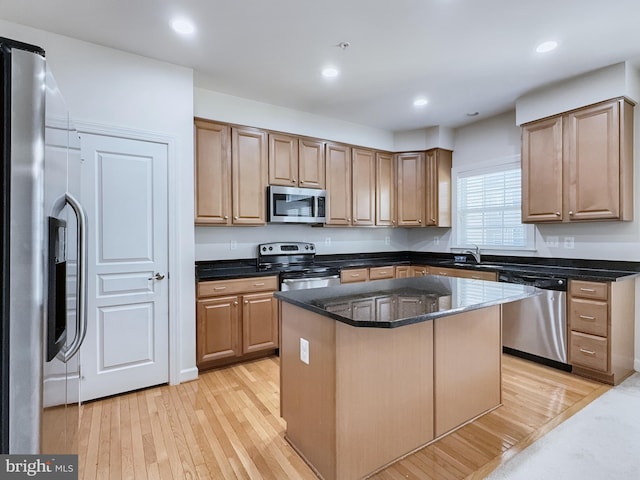 kitchen with a kitchen island, appliances with stainless steel finishes, light wood-type flooring, and dark stone counters