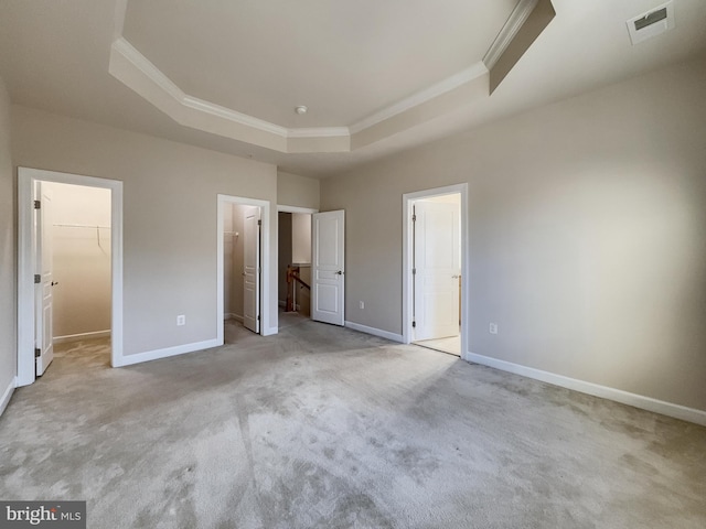 unfurnished bedroom with connected bathroom, a closet, light carpet, a spacious closet, and a raised ceiling