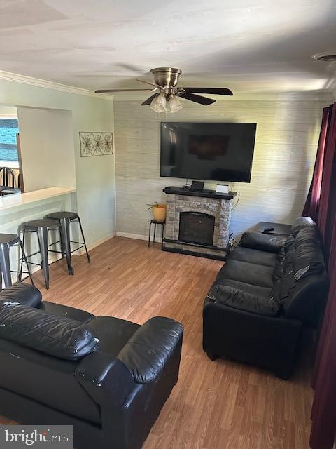 living room with crown molding, a fireplace, wood-type flooring, and ceiling fan