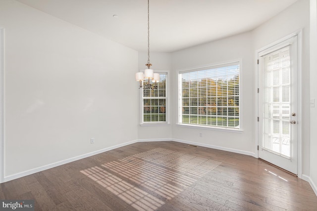 unfurnished dining area with dark wood-type flooring, a notable chandelier, and a wealth of natural light