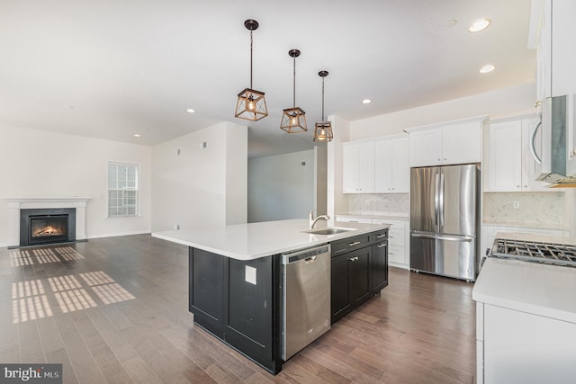 kitchen with appliances with stainless steel finishes, white cabinetry, pendant lighting, dark wood-type flooring, and a kitchen island with sink