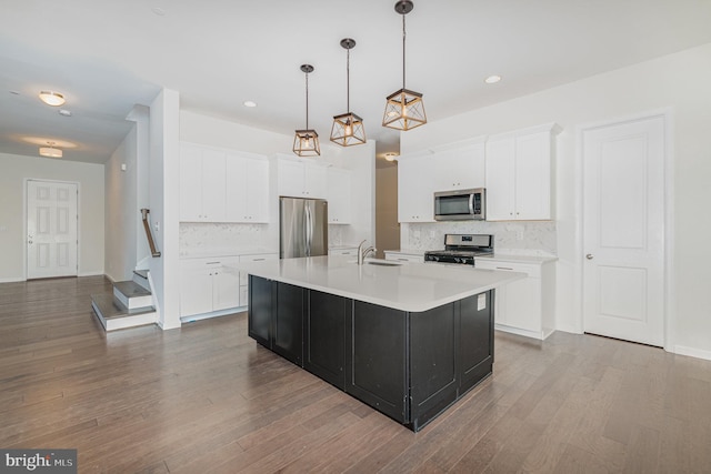 kitchen with white cabinets, a center island with sink, appliances with stainless steel finishes, hardwood / wood-style flooring, and pendant lighting