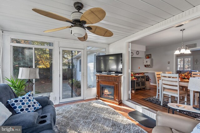 living room with ceiling fan with notable chandelier, wood ceiling, wood-type flooring, and a healthy amount of sunlight