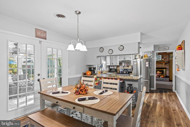 dining space featuring a notable chandelier, wood-type flooring, and a brick fireplace