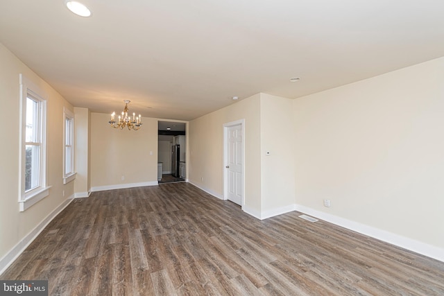 spare room with dark hardwood / wood-style floors and an inviting chandelier