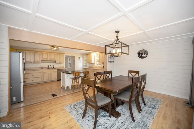 dining area with coffered ceiling, sink, a notable chandelier, light wood-type flooring, and wood walls