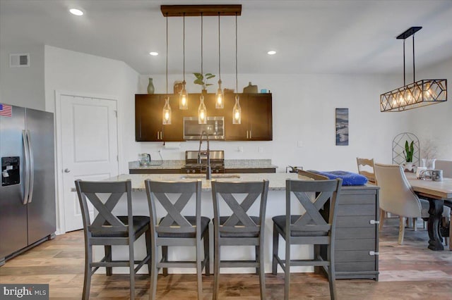 kitchen featuring a breakfast bar, stainless steel appliances, light hardwood / wood-style flooring, and an island with sink