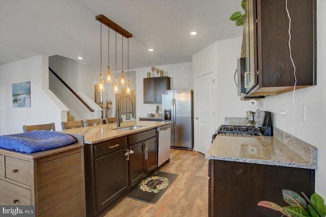 kitchen featuring sink, stainless steel appliances, pendant lighting, a center island with sink, and light wood-type flooring