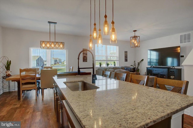 kitchen with pendant lighting, dark hardwood / wood-style floors, light stone countertops, and sink