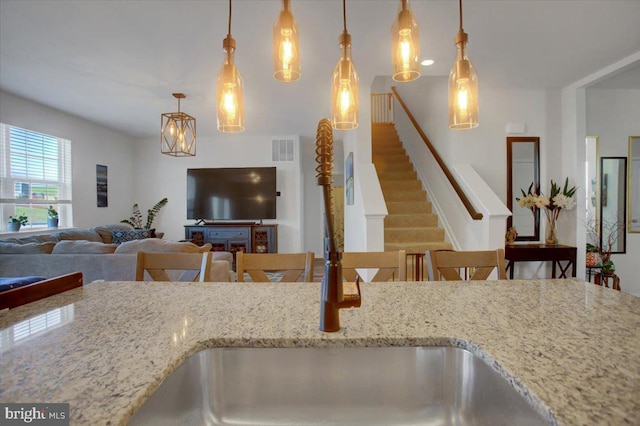 kitchen featuring a kitchen bar, light stone counters, and decorative light fixtures