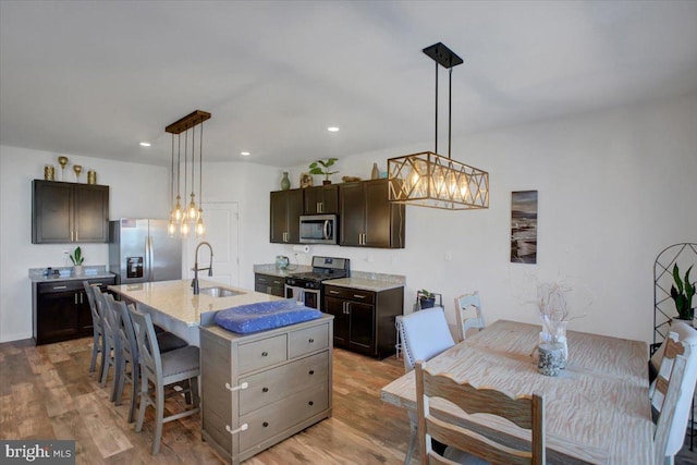 kitchen with dark brown cabinetry, light wood-type flooring, an island with sink, and appliances with stainless steel finishes